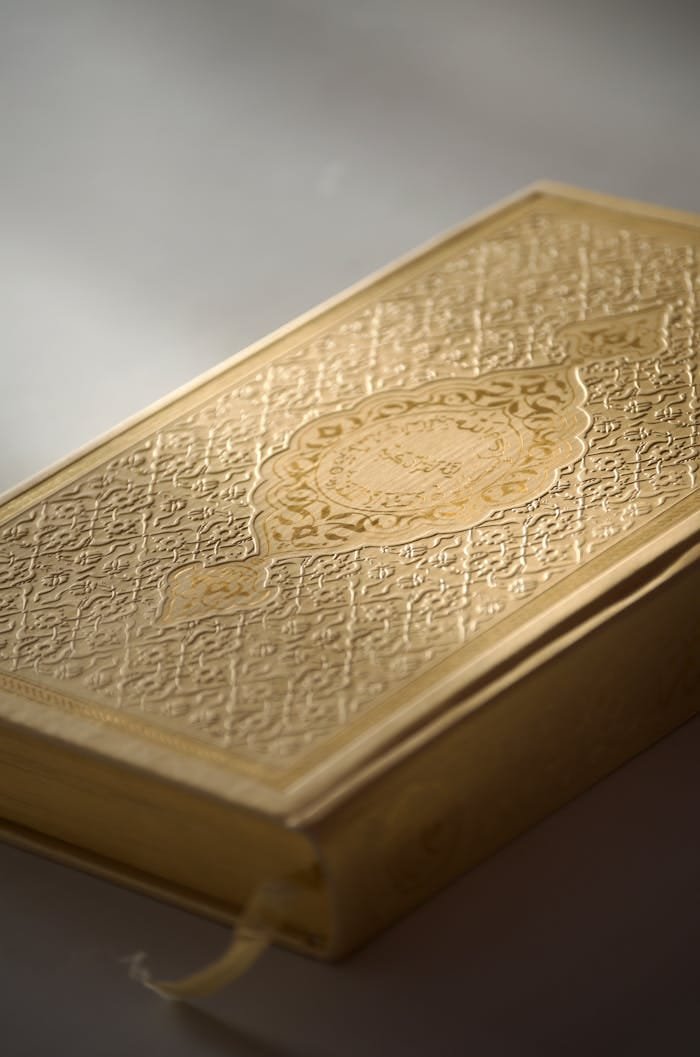 Close-up of an ornate religious book with a gold cover on a gray background, highlighting intricate details.