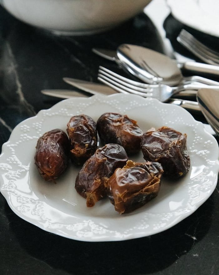 A stylish still life of dates on a white plate with cutlery, perfect for Ramadan or dessert themes.